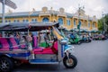 A tricycle tuk-tuk waits for tourists in front of an ancient yellow building in Bangkok