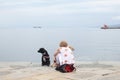 Trieste, September 5 2017, Italy: an adult woman sitting on a stone pier with two dogs