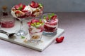 Trifles in layers with red plums and whipped cream in dessert, portioned glasses.