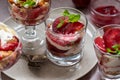 Trifles in layers with red plums and whipped cream in dessert, portioned glasses.