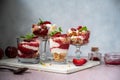 Trifles in layers with red plums and whipped cream in dessert, portioned glasses.