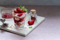 Trifles in layers with red plums and whipped cream in dessert, portioned glasses.