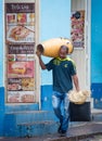 Man walks down street carrying his drum on his shoulder and hat