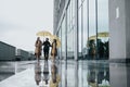 Trio of business partners with yellow umbrellas walking in rainy urban setting.