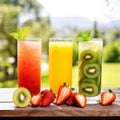 Trio of fresh healthy fruit juice blends in tall glasses on a summer picnic table outdoors with orange