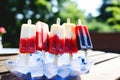 A trio of popsicles in a bowl with vibrant red, white, and blue toppings., Red, white, and blue popsicles on an outdoor table, AI