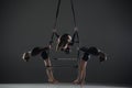 Trio of young female acrobats posing on a cube suspended at a height. Aerial gymnasts perform in studio against dark