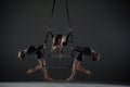 Trio of young female acrobats posing on a cube suspended at a height. Aerial gymnasts perform in studio against dark