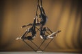 Trio of young female acrobats posing on a cube suspended at a height. Aerial gymnasts perform in a studio with yellow