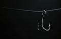 Triple fishing hook hangs on dark background line. Sharp metallic object with pointy ends, ready for angling bait. Symbolizes risk Royalty Free Stock Photo