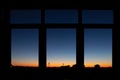 Through triple window POV with scenic city downtown cityscape black building silhouettes against fiery orange to blue