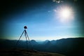 Tripod with red baseball cap on the peak ready for photography. Sharp autumn rocky peaks increased from heavy fog.