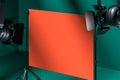 Tripods Holding Blank Orange Poster Illuminated By Spotlights In Photo Studio With Green Background. 3D Rendering.