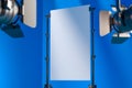 Tripods Holding Blank White Poster Illuminated By Spotlights In Photo Studio With Blue Background. 3D Rendering.