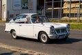 A Triumph Herald Coupe is driving along the city street.