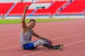 Triumphant Asian athlete with prosthetics sits post-practice on track, raising finger, symbolizing victory