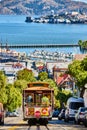 Trolley going down steep, sunny road with Alcatraz Island in San Francisco Bay, CA