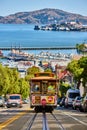 Trolley streetcar going down steep, sunny road with Alcatraz Island in San Francisco Bay, CA