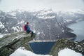 Trolltunga cliff under snow in Norway. Scenic Landscape. Man traveller sitting on edge of rock and looking at distance Royalty Free Stock Photo