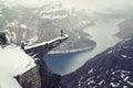 Trolltunga cliff under snow in Norway. Scenic Landscape. Man traveller standing on edge of rock and looking down. Travel Royalty Free Stock Photo