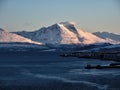 Troms region. Rocky coast of fjord in winter with snow and ice. Snowy mountains and fishing village in the background Royalty Free Stock Photo