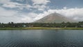 Tropic volcano at lake coast aerial. Tourist cruise at boat at green grass valley at shore