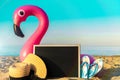 Tropical background. Funny pink toy flamingo with blackboard, slippers and hat for text on summer ocean nature beach background in Royalty Free Stock Photo