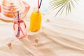 Tropical beach fruit cold strawberry and orange cocktail in glass bottle with straw, sun hat, toy under green palm leaf in sun. Royalty Free Stock Photo