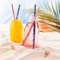 Tropical beach fruit cold strawberry and orange cocktail in wet glass bottle with straw, sun hat under green palm leaf in sun beam Royalty Free Stock Photo