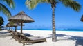 Tropical beach with palm trees and white sand blue ocean and beach beds with umbrella,Sun chairs and parasol under a Royalty Free Stock Photo