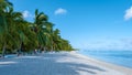 Tropical beach with palm trees and white sand blue ocean and beach beds with umbrella,Sun chairs and parasol under a Royalty Free Stock Photo