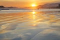 Sea with small waves, sand on the beach, mountains in the background, clouds from the sky, the sun sets, reflections in water and
