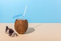 Tropical cocktail in coconut with straw and an umbrella, on paper blue and yellow background. The concept of relaxation, summer Royalty Free Stock Photo