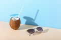 Tropical cocktail in coconut with straw and an umbrella, on paper blue and yellow background. The concept of relaxation, summer Royalty Free Stock Photo