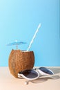 Tropical cocktail in coconut with straw and an umbrella, on paper blue and yellow background. The concept of relaxation, summer Royalty Free Stock Photo