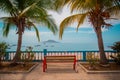 Tropical dreams, picturesque palms surrounding a red bench with a view towards an islands and a beach with boats. Beautiful