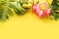 Tropical frame of fruits, banana, lime, leaves palms, orange juice in inflatable pink flamingo on punchy pastel yellow background
