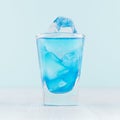 Tropical fresh alcohol cocktail with blue curacao liqueur, ice cube in frozen shot glass on soft light white, pastel green wall. Royalty Free Stock Photo