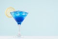 Tropical fresh alcohol cocktail with blue curacao liqueur, ice cube, lemon slice in misted martini glass on soft light white. Royalty Free Stock Photo