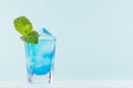 Tropical fresh blue shot drink with curacao, ice cubes, green mint in exquisite misted shot glass on pastel green wall, white wood Royalty Free Stock Photo