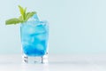 Tropical fresh cocktail with blue curacao liqueur, ice cube, sugar rim, green mint in frozen shot glass on soft light white.