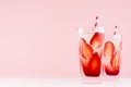 Tropical fresh strawberry cocktail with ice cubes, pieces berry and striped red straw on pastel pink background.