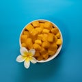 Tropical fruit concept. Yellow mango cube slices in white bowl on bright blue background with white flower. Flat lay Royalty Free Stock Photo