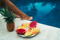 Tropical fruits lie in a plate near the feet of the girl. Dragon fruity, papaya, passion fruit, mango on the background