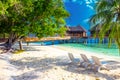 Tropical island with sandy beach, palm trees, overwater bungalows and tourquise clear water.