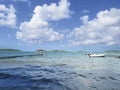 Wooden jetty in turquoise waters with waves. Blue sky with white Caribbean clouds. White boat moored. Tropical landscape