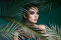 Tropical portrait sexy woman in leaves palm tree. Bright green makeup, shadow of palm leaves on girl face. Beautiful makeup