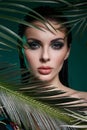 Tropical portrait sexy woman in leaves palm tree. Bright green makeup, shadow of palm leaves on girl face. Beautiful makeup