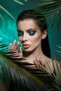 Tropical portrait sexy woman in leaves palm tree. Bright green makeup, shadow of palm leaves on girl face. Beautiful makeup