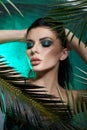 Tropical portrait sexy woman in leaves palm tree. Bright green makeup, shadow of palm leaves on girl face. Beautiful makeup